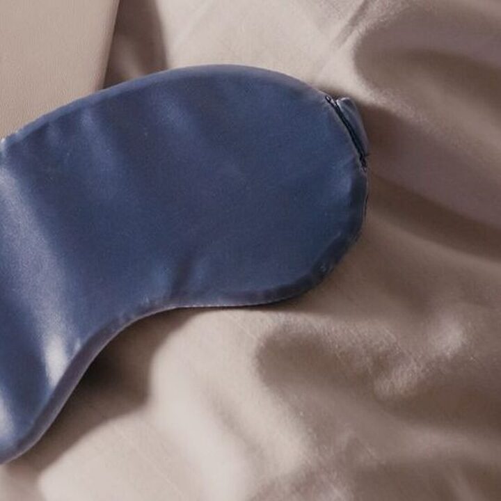Navy silk sleep mask resting on bedding